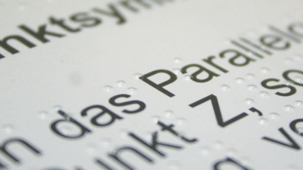 Das Foto mit Unschärfen in den Randbereichen zeigt einen Textausschnitt, in dem am der Wortteil Parallel zu erkennen ist. Es geht um ein Parallelogramm.  Der mathematische Lehrtext ist mit erkennbaren Braillepunkten zusätzlich zum gedruckten Text versehen. Bildnachweis: Anna Hielscher